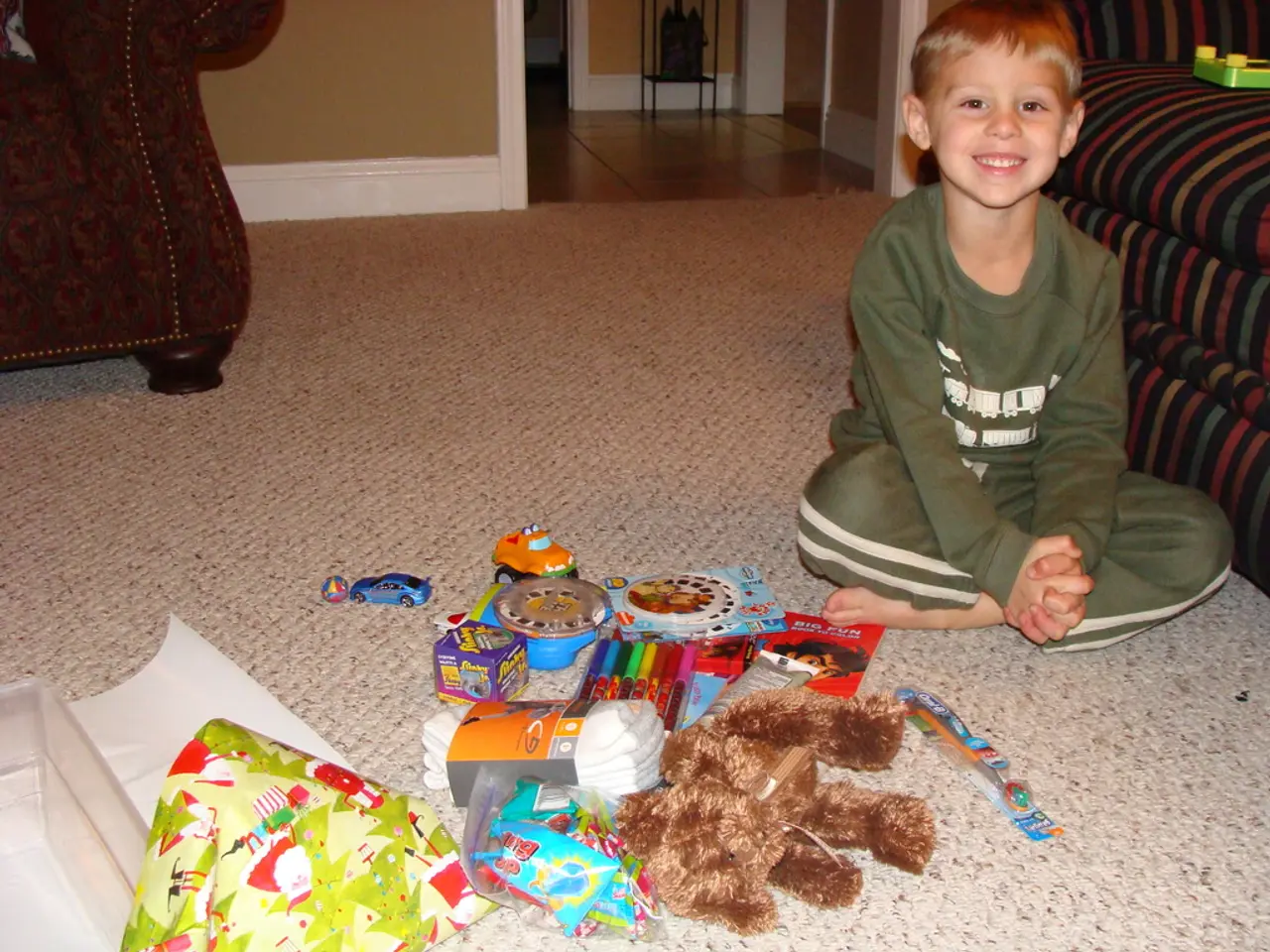 There is a boy sitting on a mat and smiling, beside him we can see toy on a sofa. We can see doll,...
