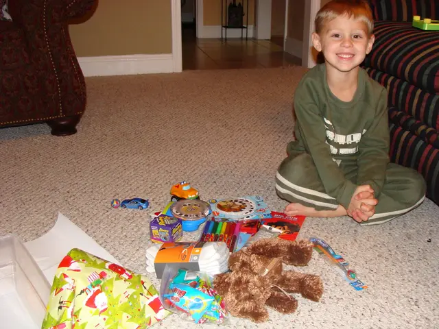 There is a boy sitting on a mat and smiling, beside him we can see toy on a sofa. We can see doll,...