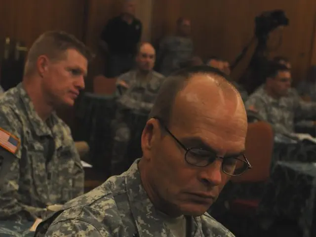 In this picture, there are men sitting on the chairs and they are wearing uniforms. The man in the...