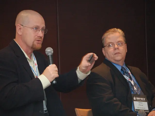 Here we can see a couple of men sitting on chairs and the guy on the left side is speaking...